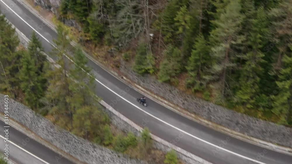Aerial tracking shot of man riding fast a motorcycle on mountain highway. Motorcycle rider racing his motorcycle on country road. Young man riding motorbike on trip. Concept of freedom and adventure Aerial tracking shot of man riding fast a motorcycle on mountain highway. Motorcycle rider racing his motorcycle on country road. Young man riding motorbike on trip. Concept of freedom and adventure