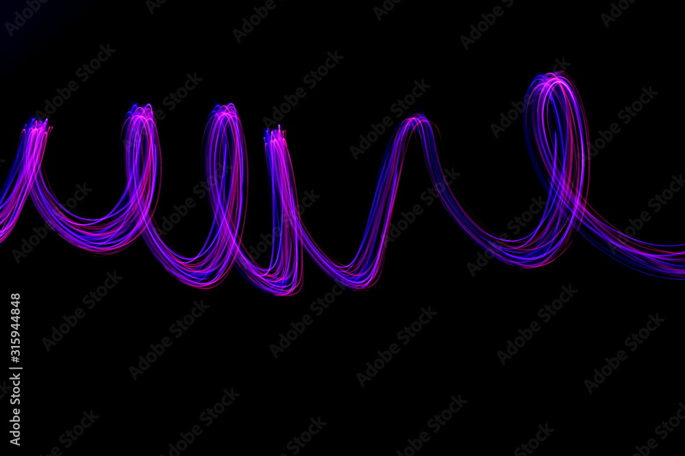 Long exposure light painting, vibrant purple color in abstract swirl against a clean black background. Light painting photography. Long exposure light painting, vibrant purple color in abstract swirl against a clean black background. Light painting photography.