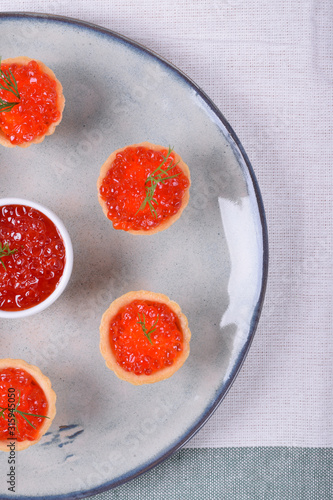 Red caviar served in shortbread tartlets and a ceramic bowl topped with dill on the round plate
