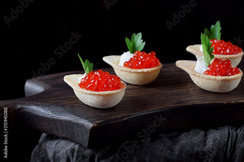 Red caviar and ricotta cheese in the spoon shaped tartlets served on the wooden board