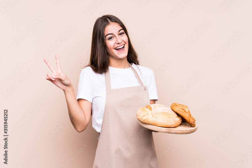 Young caucasian baker woman isolated joyful and carefree showing a peace symbol with fingers. Young caucasian baker woman isolated joyful and carefree showing a peace symbol with fingers.