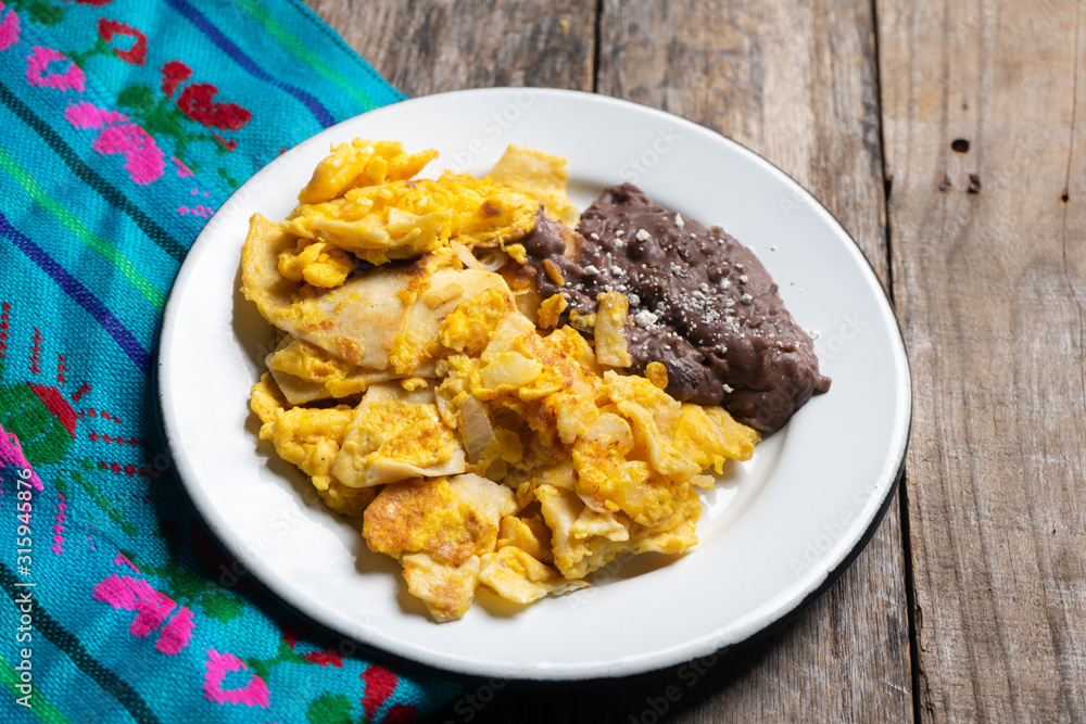 Mexican scrambled eggs with corn tortilla also called migas on wooden background