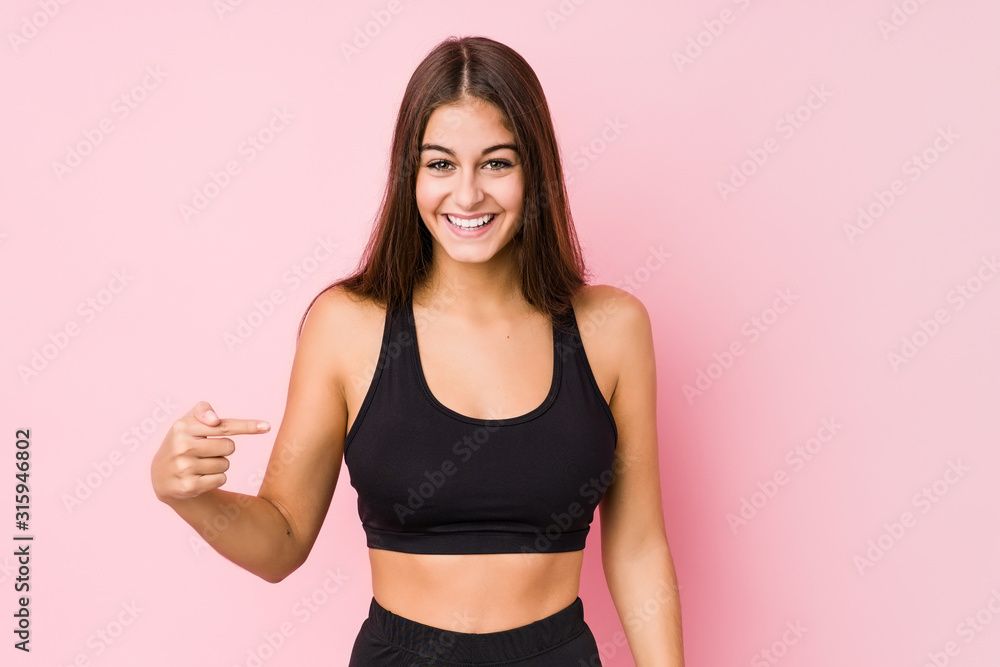 Young caucasian fitness woman doing sport isolated person pointing by hand to a shirt copy space, proud and confident