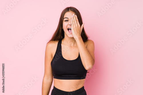 Young caucasian fitness woman doing sport isolated having fun covering half of face with palm.