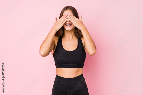 Young caucasian fitness woman doing sport isolated covers eyes with hands  smiles broadly waiting for a surprise.