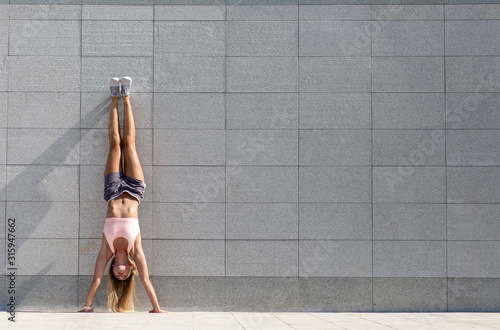 Beautiful young woman in sports wear in hand stand yoga pose exercising outdoors