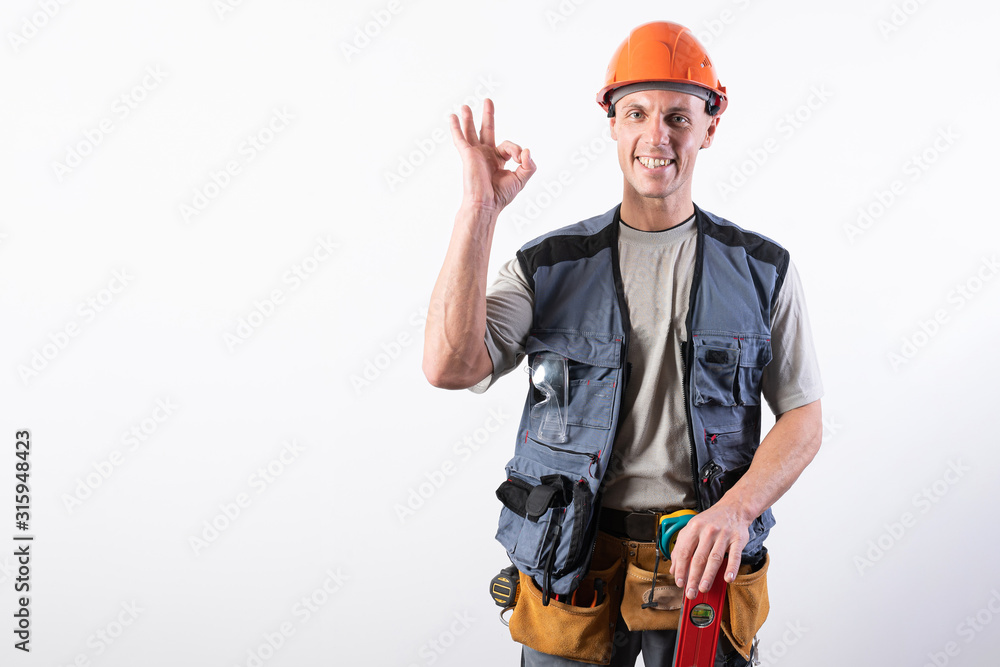 The builder shows the sign okay. In work clothes and hard hat. On a light gray background. The builder shows the sign okay. In work clothes and hard hat. On a light gray background.