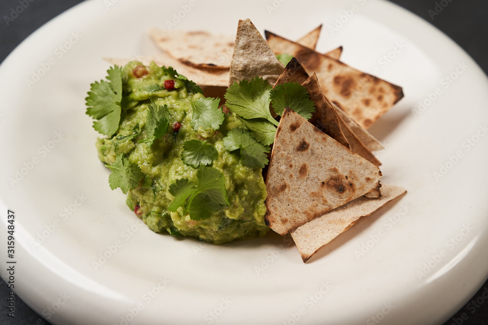 Guacamole with pita chips on white plate, close-up. Mexican guacamole Guacamole with pita chips on white plate, close-up. Mexican guacamole