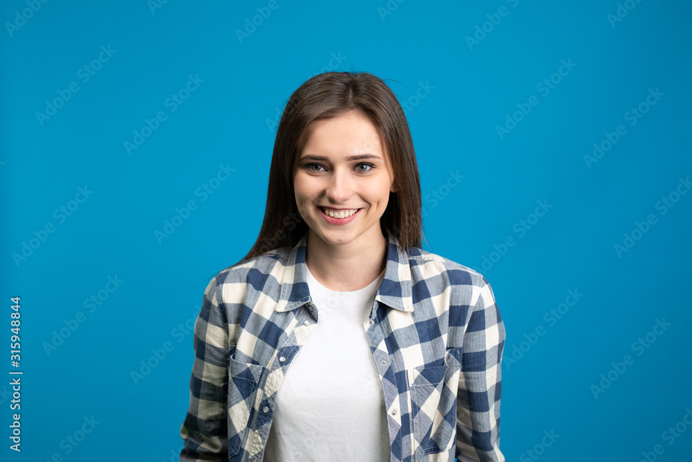 Front view of smiling girl in checkered shirt isolated on blue background Front view of smiling girl in checkered shirt isolated on blue background