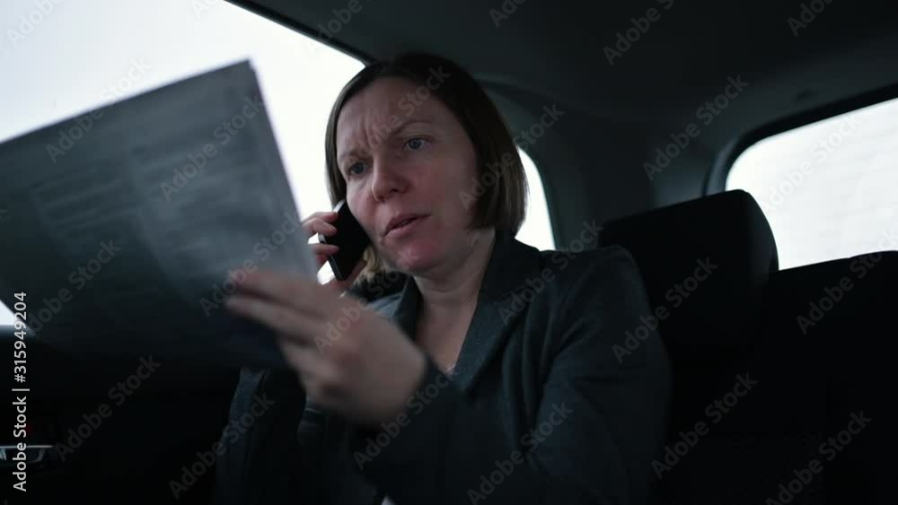 Businesswoman reading newspaper and using mobile phone at car backseat