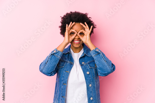 Young african american woman against a pink backgroound isolated showing okay sign over eyes © Asier