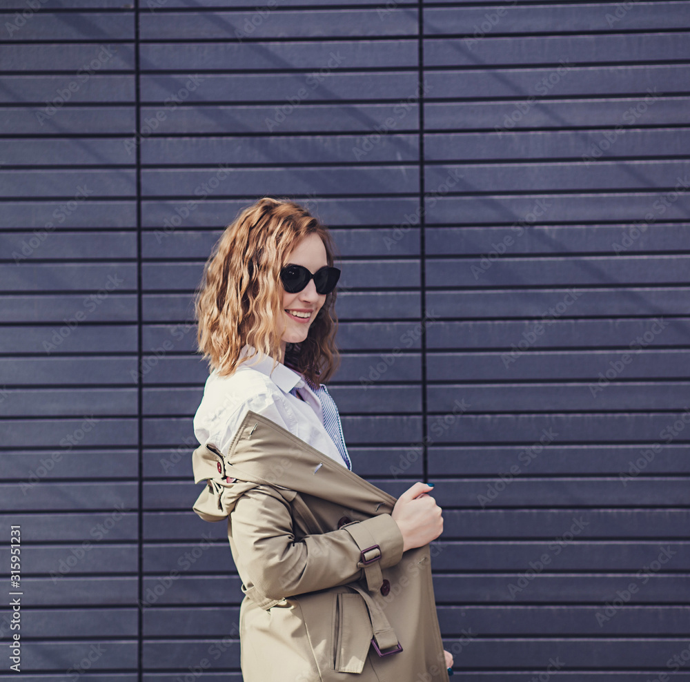 happy curly-haired woman in a jacket posing against a wall happy curly-haired woman in a jacket posing against a wall