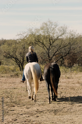 Western lifestyle shows woman riding horse while ponying bareback on ranch.