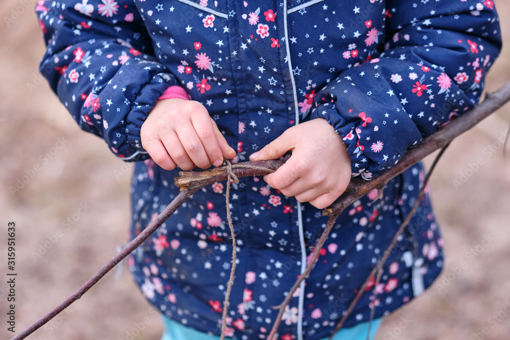 Obraz premium Closeup of midsection of a caucasian child girl in warm winter clothing playing with a wooden twig and a string and trying to make a knot. Seen in Germany in January