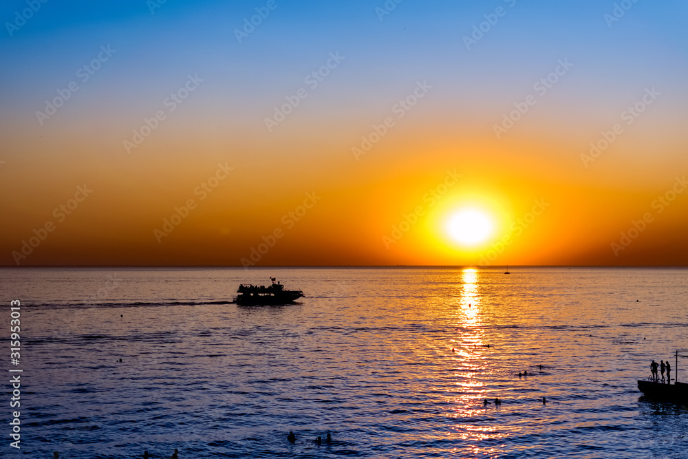 Красивый, красочный и контрастный закат над морем, океаном. Горячее солнце освещает просторный пейзаж, отбрасывая блики лучей на водную гладь. Яркий солнечный восход. Путешествие и туризм.