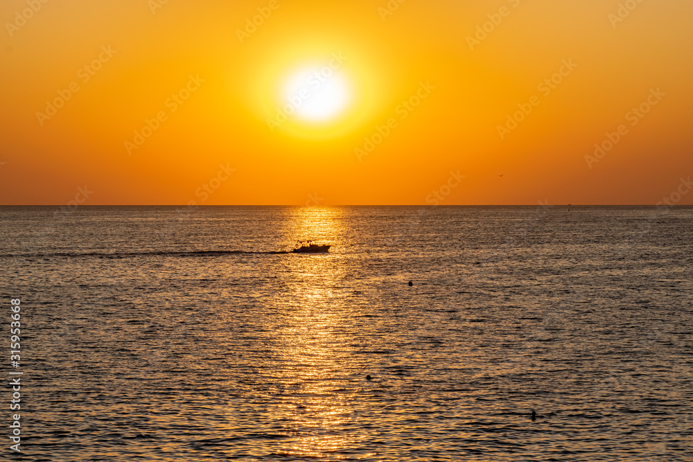 Красивый, красочный и контрастный закат над морем, океаном. Горячее солнце освещает просторный пейзаж, отбрасывая блики лучей на водную гладь. Яркий солнечный восход. Путешествие и туризм.