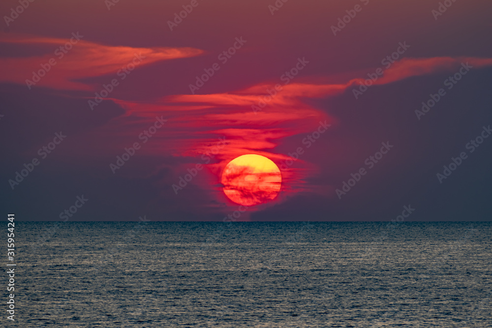 Obraz premium Красивый, красочный и контрастный закат над морем, океаном. Горячее солнце освещает просторный пейзаж, отбрасывая блики лучей на водную гладь. Яркий солнечный восход. Путешествие и туризм.