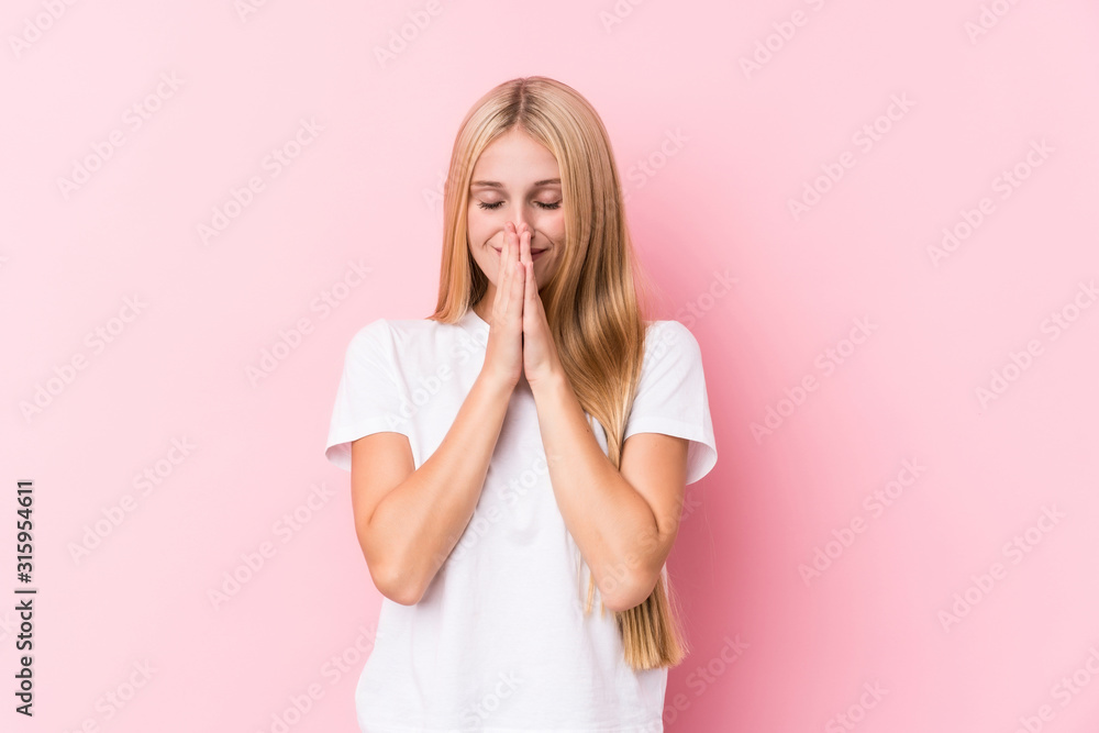 Young blonde woman on pink background holding hands in pray near mouth, feels confident. Young blonde woman on pink background holding hands in pray near mouth, feels confident.