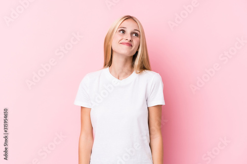 Young blonde woman on pink background dreaming of achieving goals and purposes