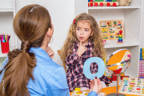 Young girl  in speech therapy office. Preschooler exercising correct pronunciation with speech therapist.