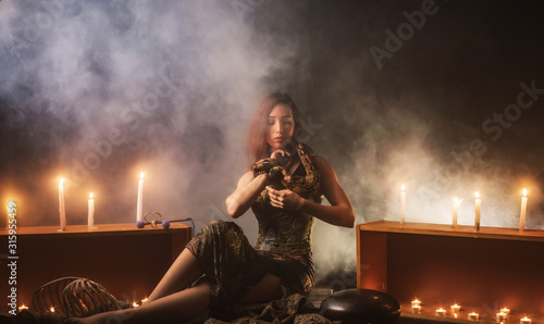 Foto a witch with a snake on her neck and in her hands sits in a haze against a backg