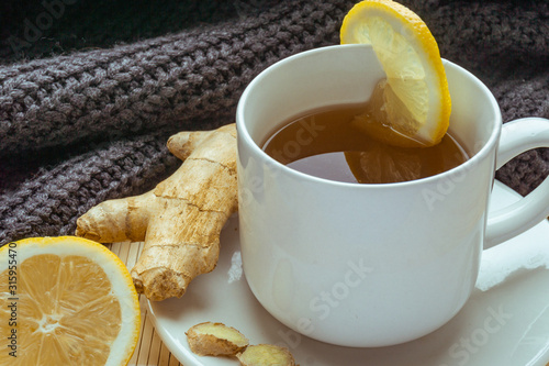 Closeup of the cup of hot ginger tea with lemon on bamboo stand with warm sweater on background. Copy space