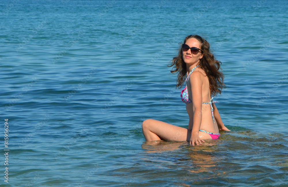 Young woman in a swimsuit and sunglasses on the seashore