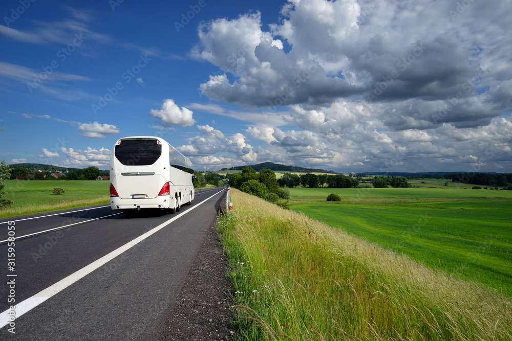 White bus driving on the asphalt road in a rural landscape