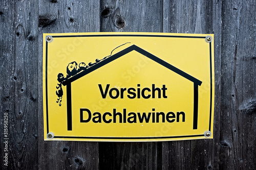 yellow sign with warning of roof avalanches bolted on a wooden barn wall, text in german language Vorsicht Dachlawinen, translated caution roof avalanches