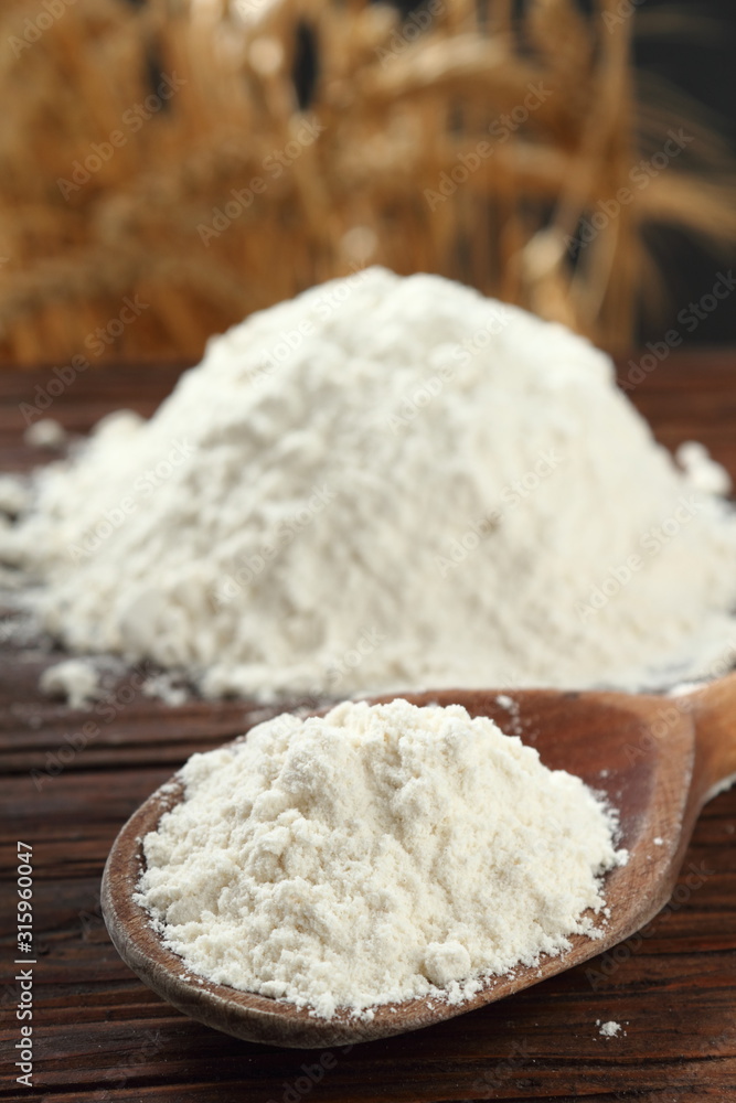 Wheat flour on wooden spoon at wheat ears background Wheat flour on wooden spoon at wheat ears background