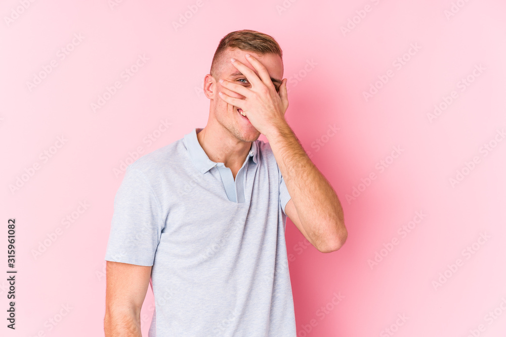 Young caucasian man isolated blink at the camera through fingers, embarrassed covering face. Young caucasian man isolated blink at the camera through fingers, embarrassed covering face.
