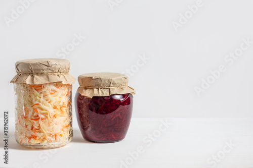 Homemade sauerkraut with carrots and cabbage salad with beets in a glass jar on a white wooden background. Fermented food.