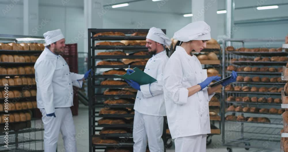 Group of charismatic bakers in a bakery section with full of fresh baked bread shelves chatting with each other , attractive lady take some notes in her new tablet Group of charismatic bakers in a bakery section with full of fresh baked bread shelves chatting with each other , attractive lady take some notes in her new tablet