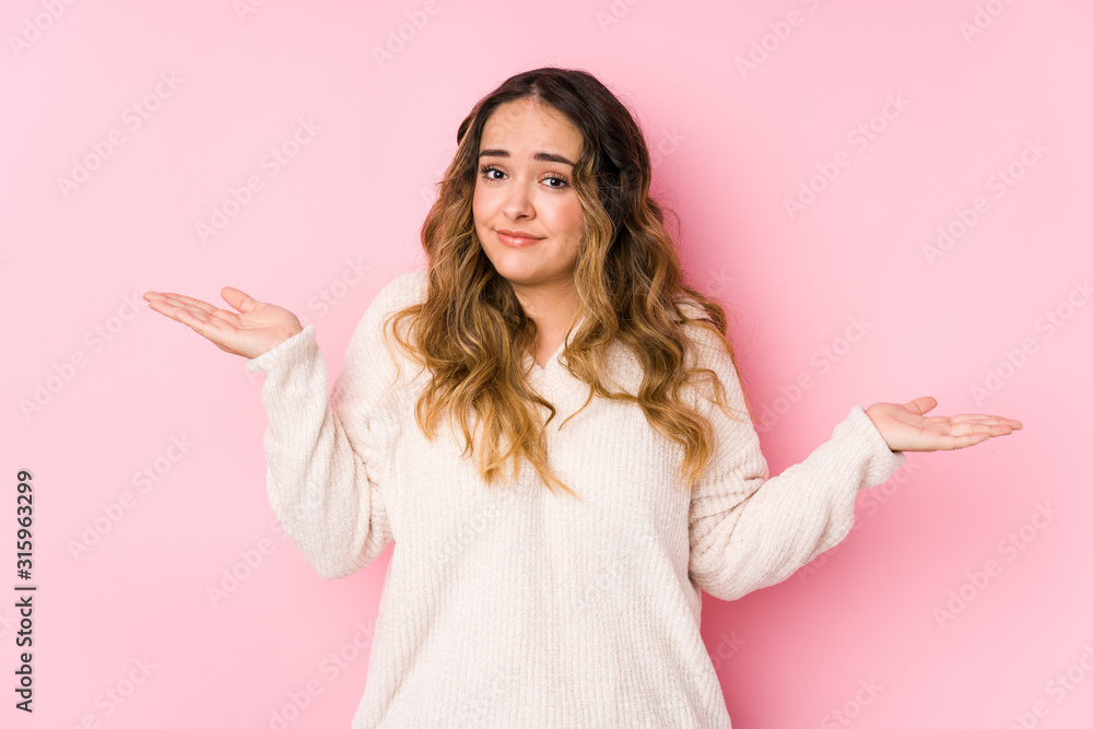 Young curvy woman posing in a pink background isolated doubting and shrugging shoulders in questioning gesture. Young curvy woman posing in a pink background isolated doubting and shrugging shoulders in questioning gesture.