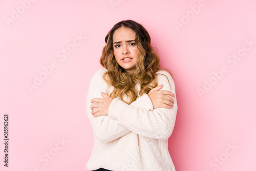 Young curvy woman posing in a pink background isolated going cold due to low temperature or a sickness. © Asier