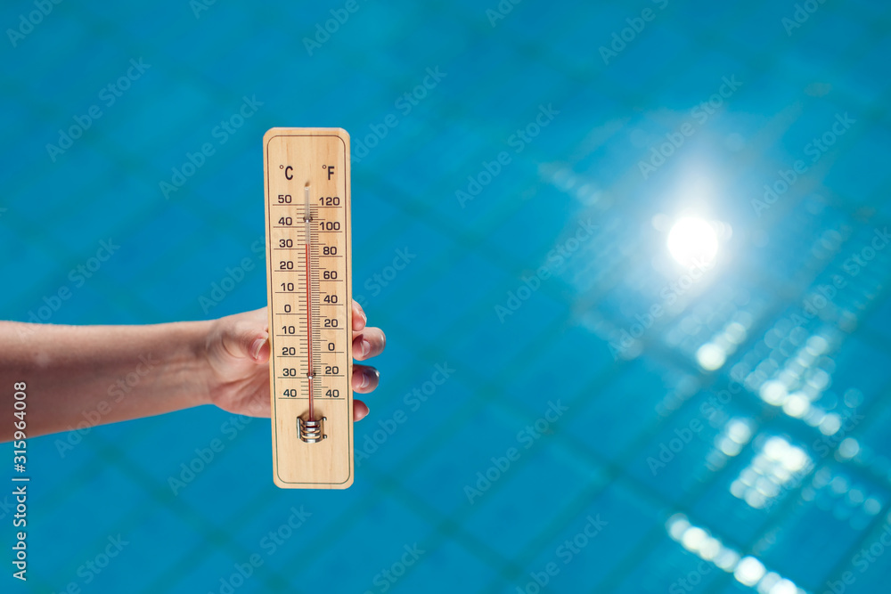 Woman holding thermometer on the pool background. Hot weather and summer concept Woman holding thermometer on the pool background. Hot weather and summer concept