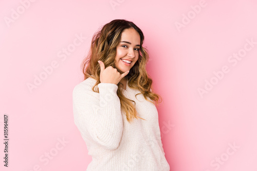 Young curvy woman posing in a pink background isolated showing a mobile phone call gesture with fingers.
