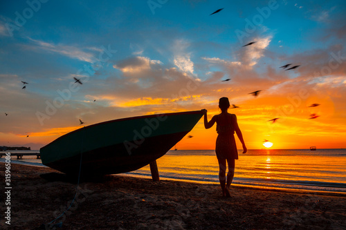 A young woman on the beach in a boat on the West End Sunset, Roatan Island with birds in the sky. Honduras