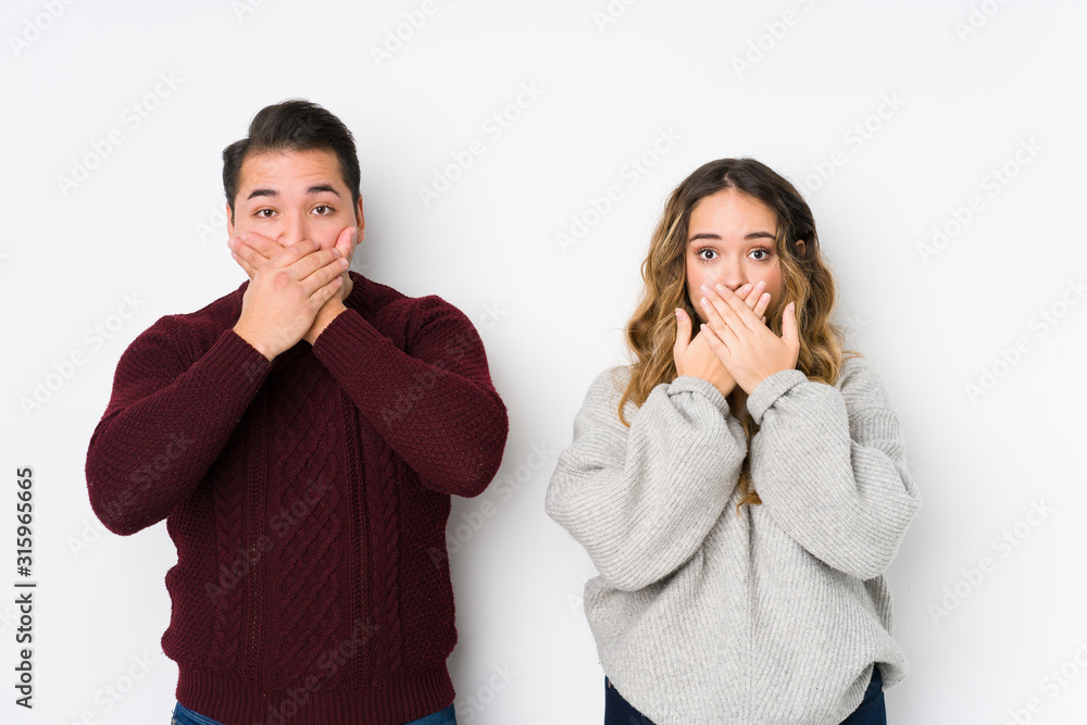 Young couple posing in a white background shocked covering mouth with hands. Young couple posing in a white background shocked covering mouth with hands.