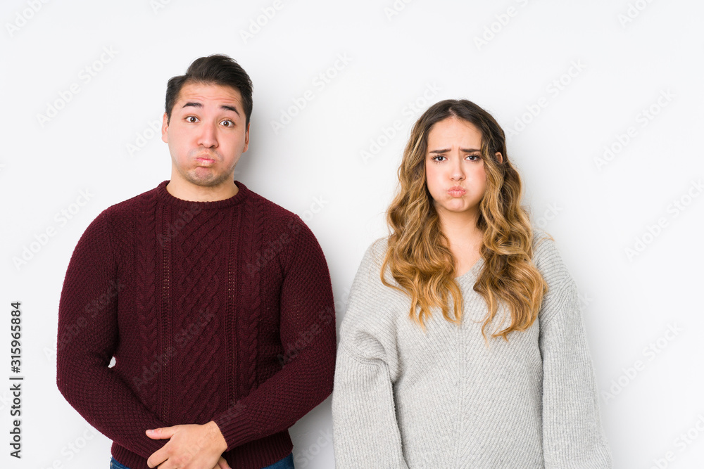 Young couple posing in a white background blows cheeks, has tired expression. Facial expression concept. Young couple posing in a white background blows cheeks, has tired expression. Facial expression concept.