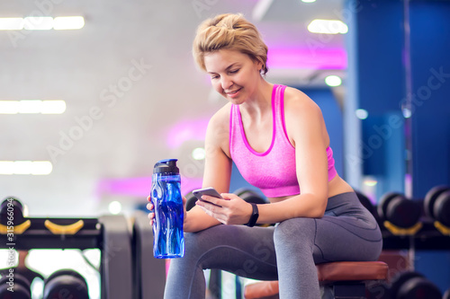 Woman resting in the gym, sitting on bench with bottle of water