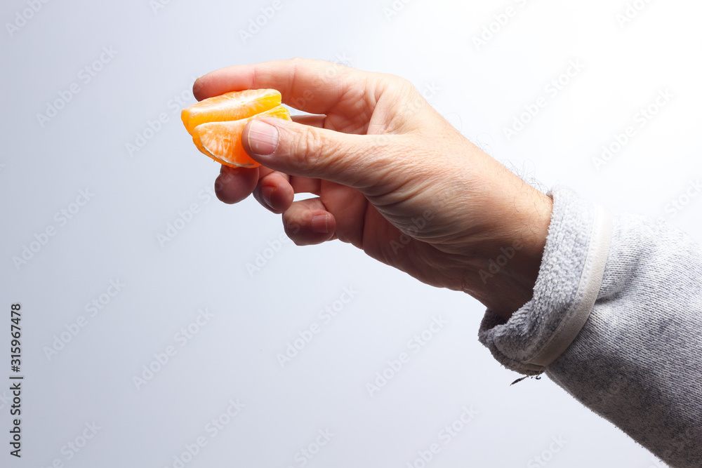 Tangerine slice in the hand of an adult person Tangerine slice in the hand of an adult person