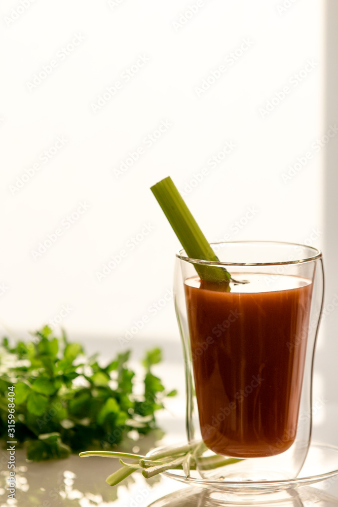 Tomato juice in a glass with celery and parsley, on a white background, close-up Tomato juice in a glass with celery and parsley, on a white background, close-up