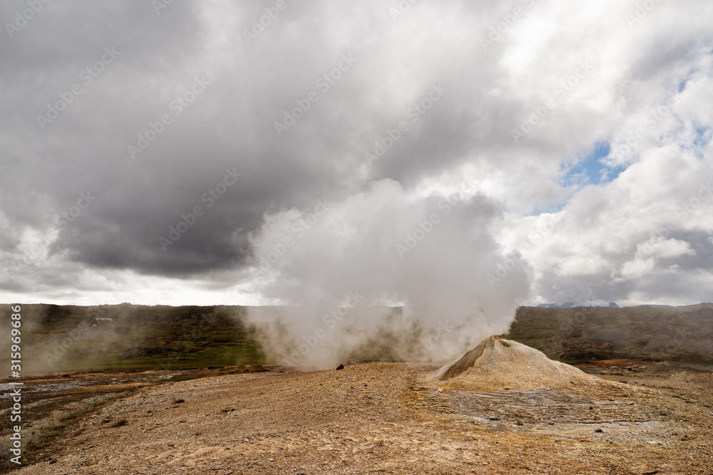 Vulkanlandschaft mit einer großen Fumarole, der viel Dampf entströmt, kontrastreicher Himmel mit etwas Blau sowie weißen und grauen Wolken - Location: Island, Hochland