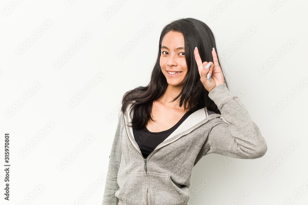 Young fitness chinese woman showing a horns gesture as a revolution concept. Young fitness chinese woman showing a horns gesture as a revolution concept.