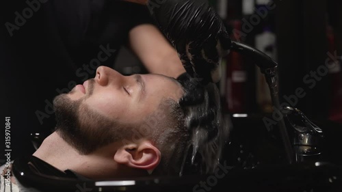 Handsome bearded man getting his hair washed at barber shop