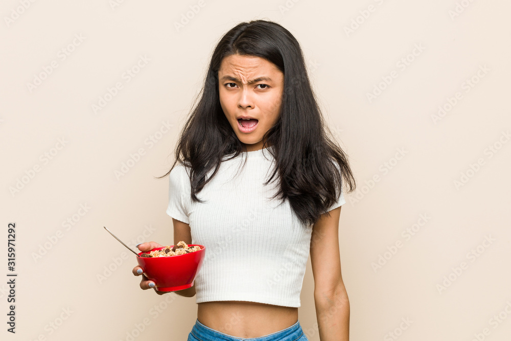 Young asian woman holding a cereals bowl screaming very angry and aggressive. Young asian woman holding a cereals bowl screaming very angry and aggressive.