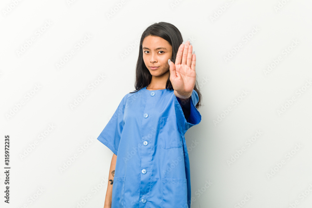 Young asian nurse woman standing with outstretched hand showing stop sign, preventing you. Young asian nurse woman standing with outstretched hand showing stop sign, preventing you.