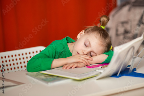 little cute girl of 7 years old, first grader, left-hander does homework at the table, homework and fell asleep at her desk on notebooks