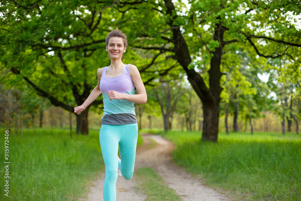 A young sports girl running in a quit green summer forest. Sport and wellness